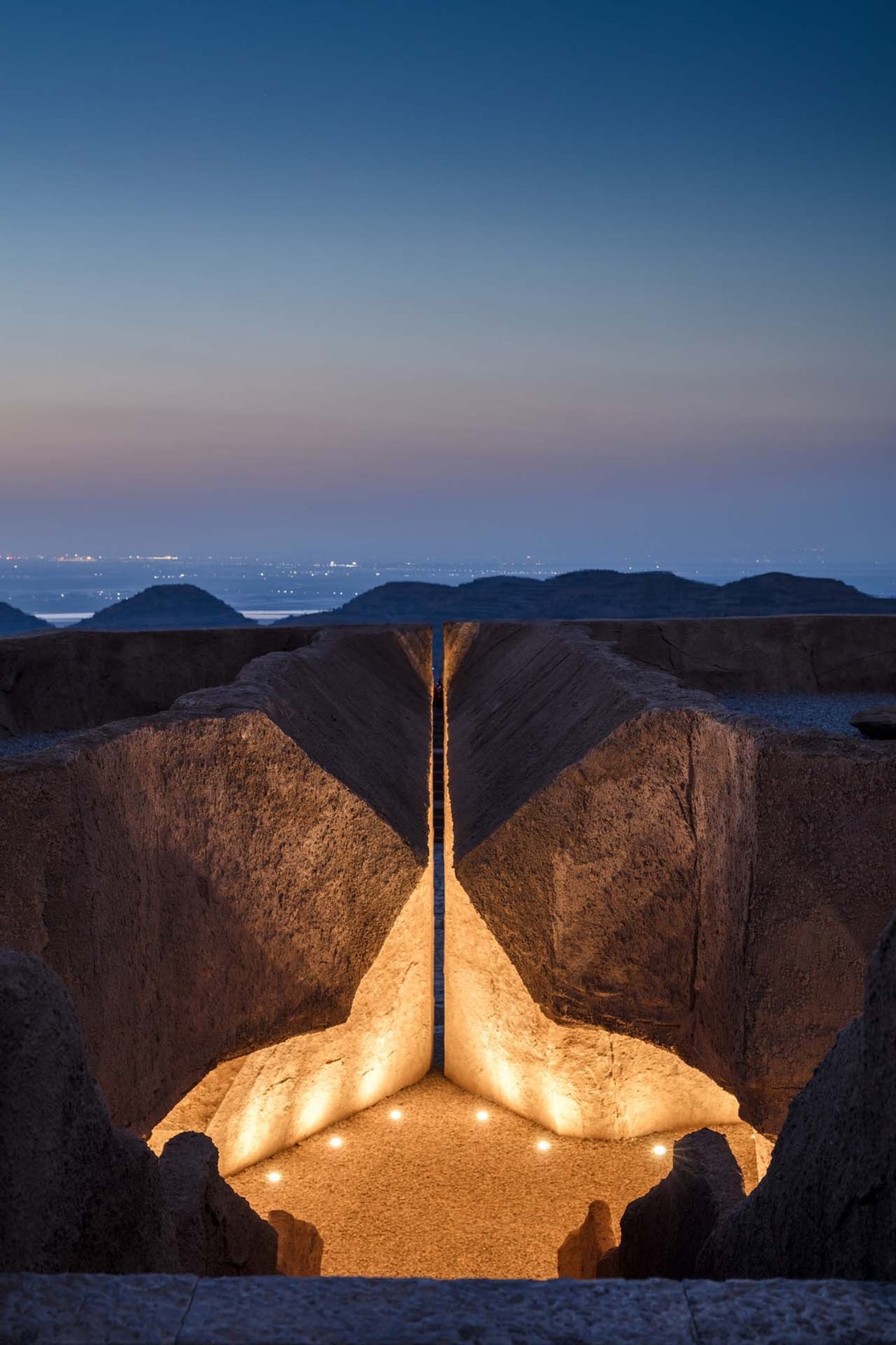 Holy Fire Lit Place in China by URBANUS — Monolithic rammed-earth excavation frames a central void carved to resemble an inverted tree form, with radiating branch-like apertures directing zenithal...