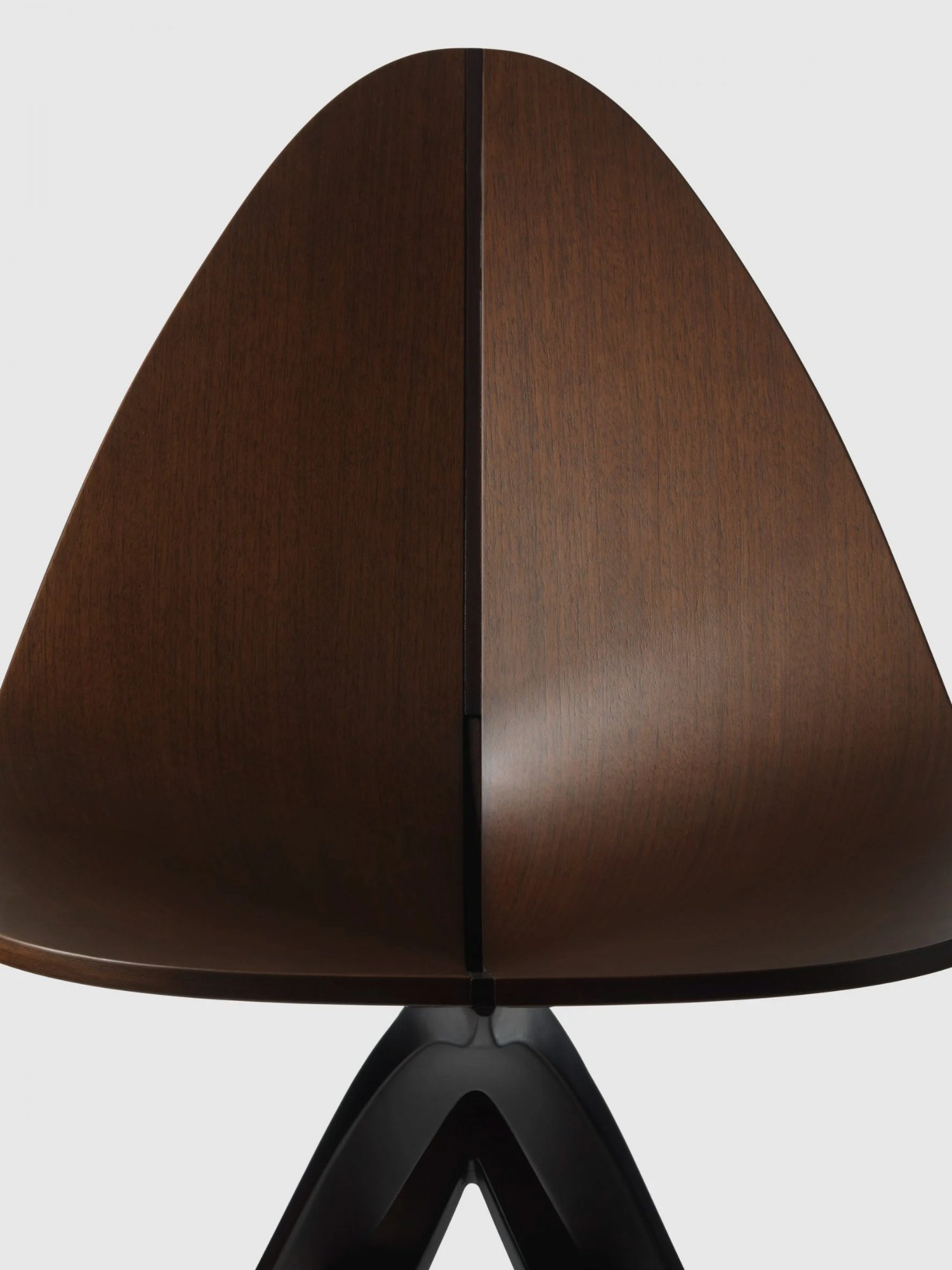 Edaha chair by GamFratesi for Koyori — Overhead view of the Edaha chair revealing its defining formal contrast: a curved veneer-covered seat in warm walnut tones with visible wood grain, bisected...