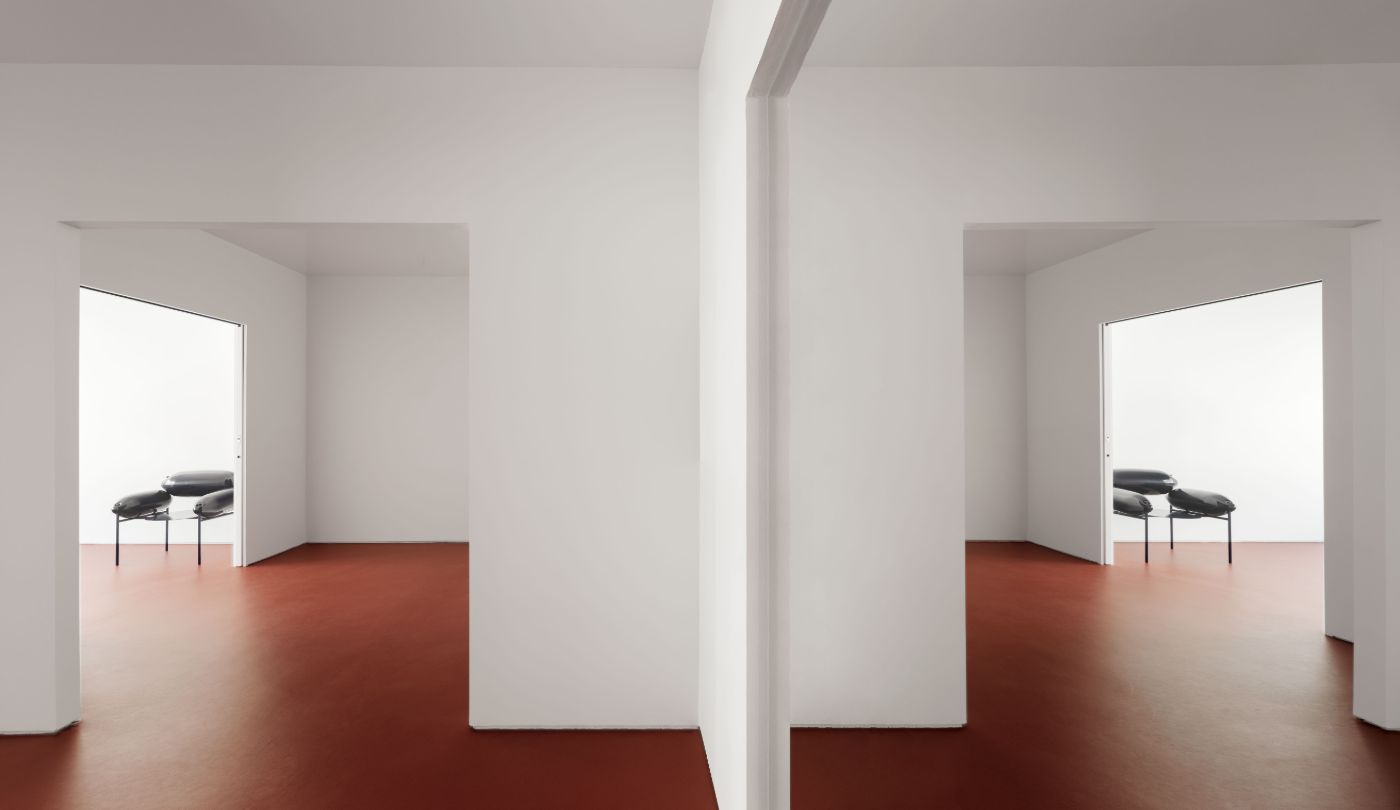 Lara House by HANGHAR — A symmetrical corridor bisected by a central white structural column frames two identical rooms with terracotta-red linoleum flooring and white walls.
