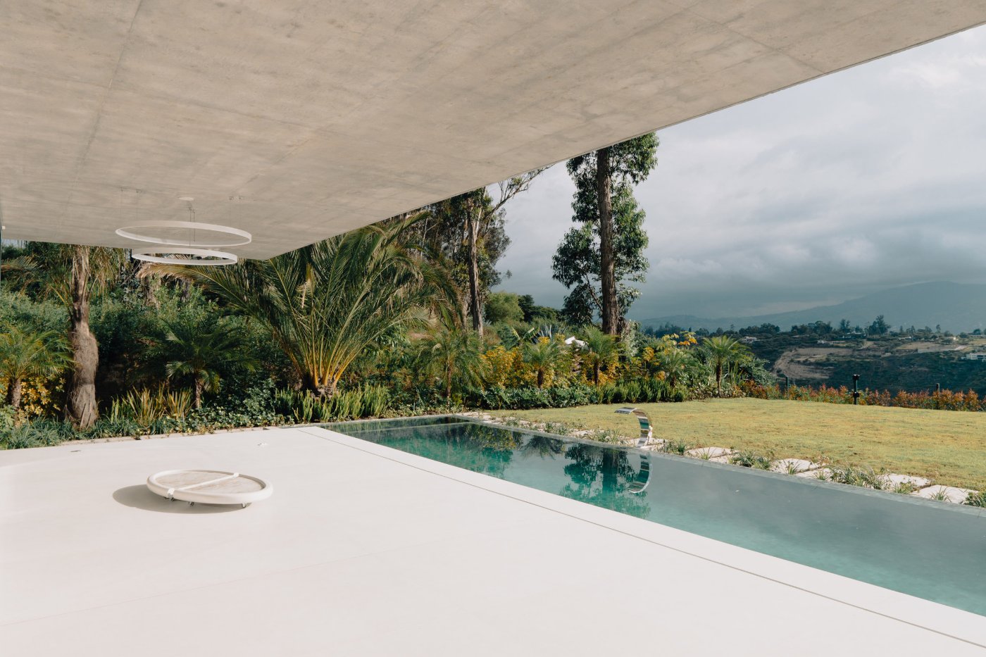 Magnolia House by Estudio Felipe Escudero — The poolside vantage reveals the project's defining gesture: a sweeping curved concrete soffit that extends from the interior pavilion across the threshold,...
