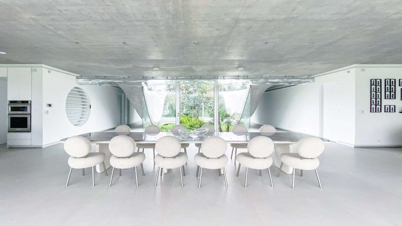 Magnolia House by Estudio Felipe Escudero — The dining pavilion centers on a monolithic concrete table beneath an undulating concrete soffit that curves overhead in sweeping, wave-like forms.