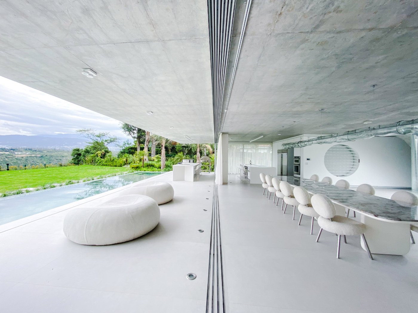 Magnolia House by Estudio Felipe Escudero — The interior opens through a continuous glass threshold onto a cantilevered concrete platform, its polished surface reflecting the sweeping soffit overhead.