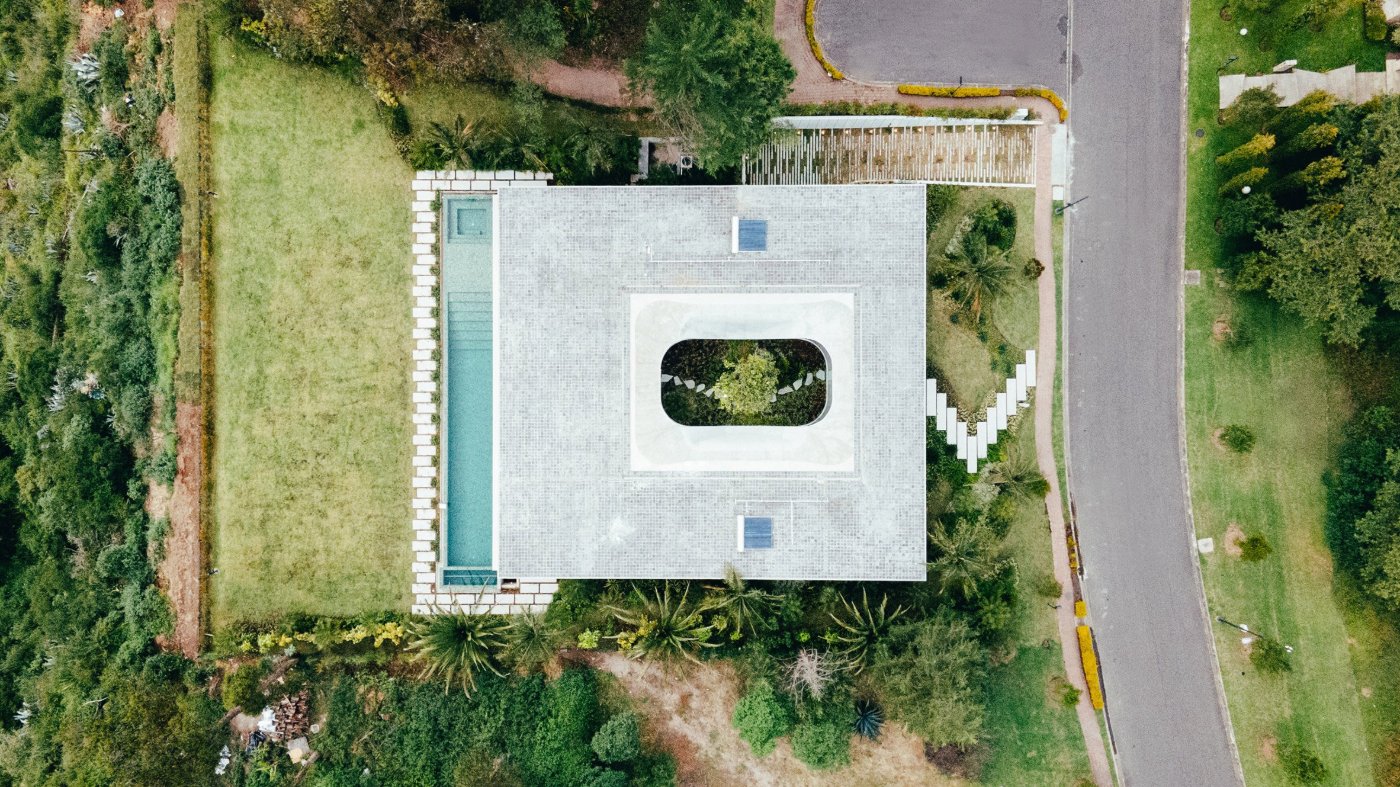 Magnolia House by Estudio Felipe Escudero — Aerial view of Magnolia House reveals the building's defining gesture: a massive curved opening cut into the white tile roof plane, framing the magnolia...