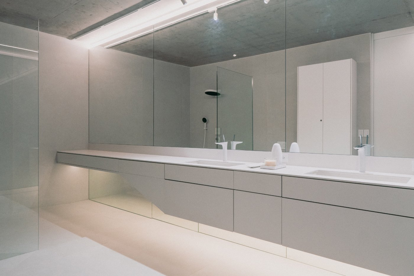 Magnolia House by Estudio Felipe Escudero — The bathroom interior showcases a minimalist approach with a continuous white countertop spanning the room's length, interrupted only by integrated sink basins.