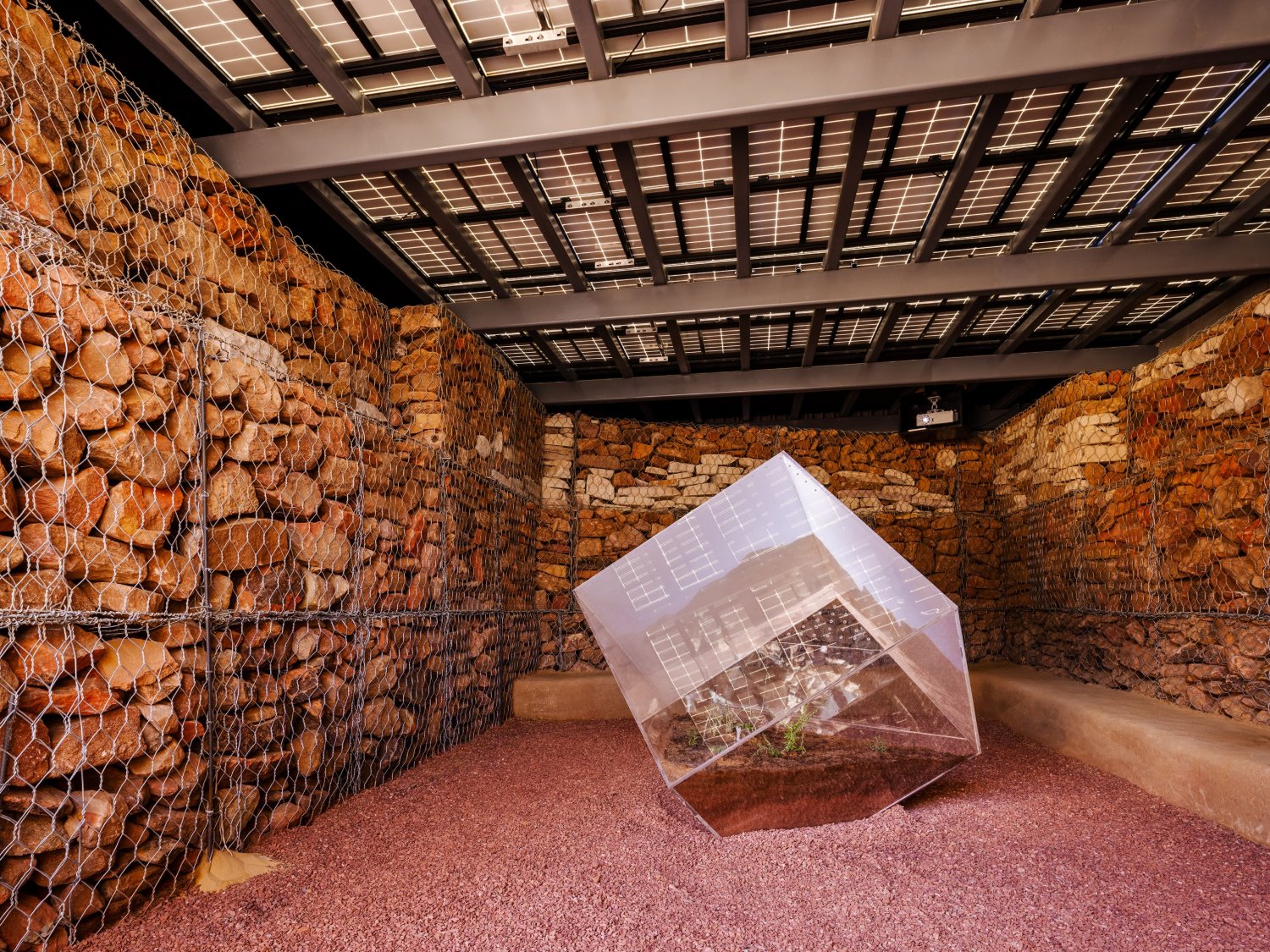 Desert X AlUla 2022 Group Exhibition — A translucent polycarbonate cubic structure dominates the sandy floor, its tilted plane topped with integrated photovoltaic panels that reference...