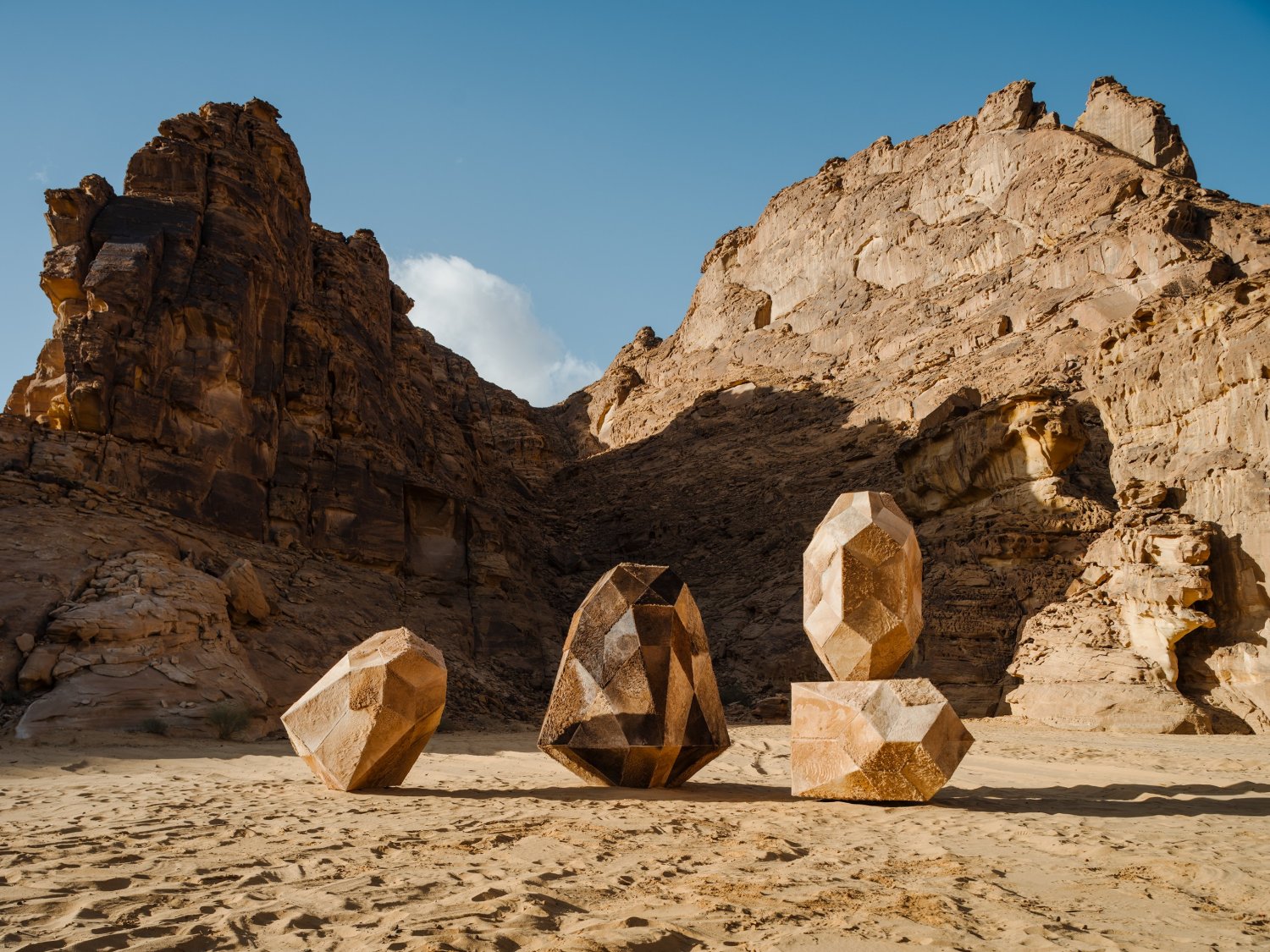 Desert X AlUla 2022 Group Exhibition — Five carved sandstone boulders with faceted, geometric surfaces occupy the desert floor of AlUla's eroded canyon.