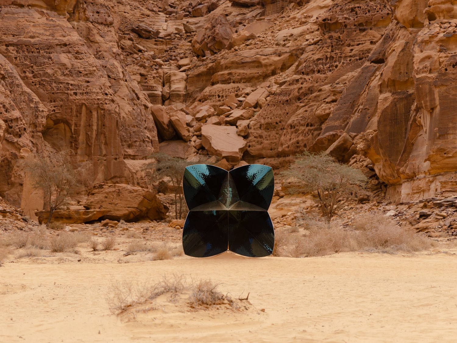 Desert X AlUla 2022 Group Exhibition — A monumental black sculptural form dominates the desert floor, its symmetrical, butterfly-like silhouette composed of four mirrored quadrants.