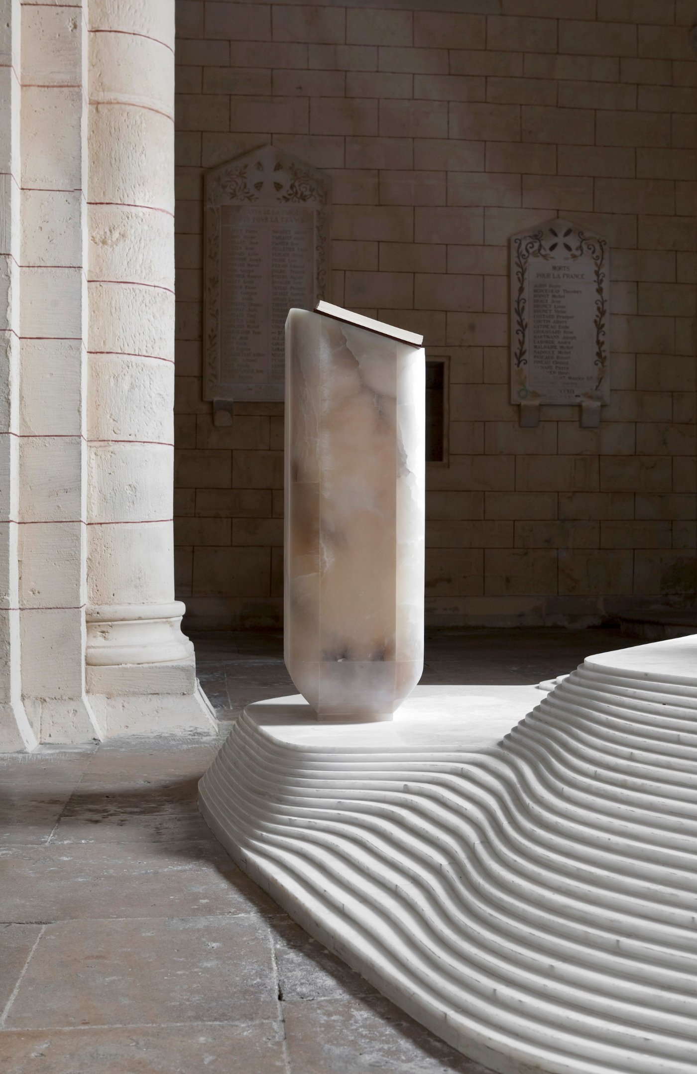 St Hilaire Church in Melle by Mathieu Lehanneur — A monolithic alabaster ambo rises centrally within the 11th-century Romanesque church, its cylindrical form carved from translucent stone with soft grey...