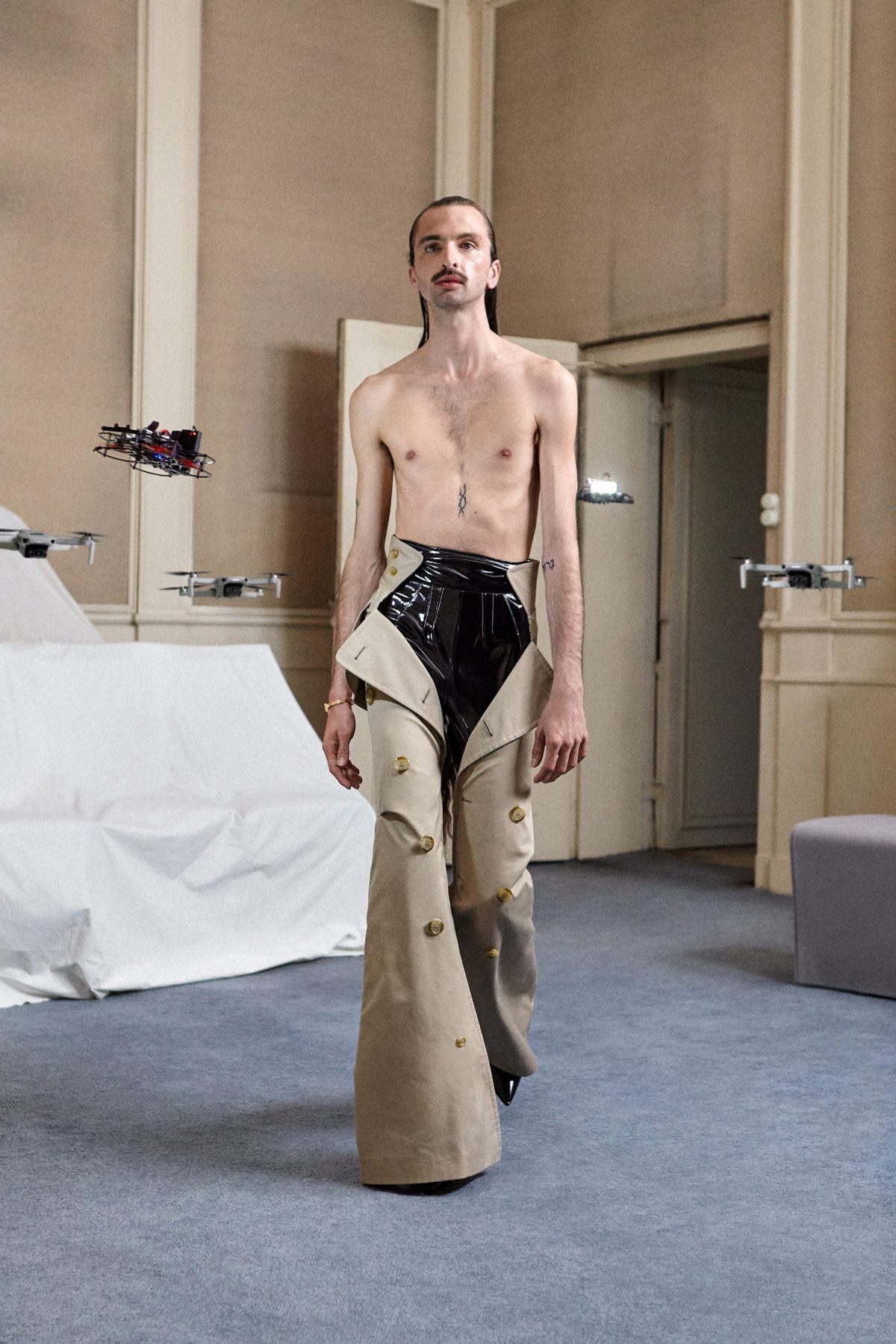 SSAW22 by Duran Lantink — A model presents a deconstructed garment combining cream-colored wool trousers with asymmetrical cutouts revealing a black knit underlay at the torso and leg.