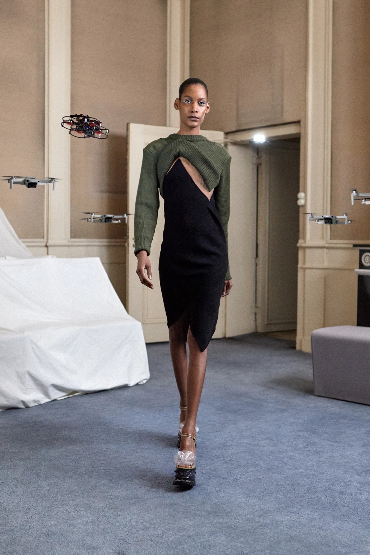 SSAW22 by Duran Lantink — A model presents a hybrid knit dress featuring an asymmetrical construction: sage-green ribbed knit on the upper torso transitions to black jersey below,...