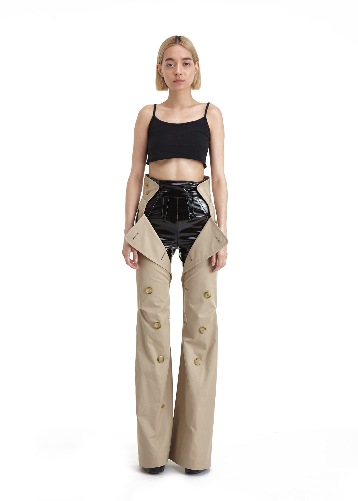 SSAW22 by Duran Lantink — A model wears a deconstructed two-piece ensemble featuring a black crop top with thin straps and cream-colored wide-leg trousers with button detailing down...