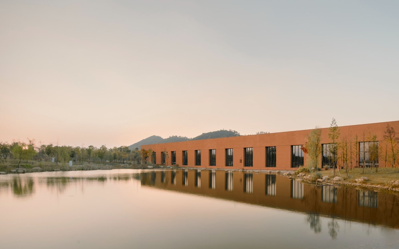 Zhejiang Museum of Natural History by David Chipperfield Architects — David Chipperfield Architects' Zhejiang Museum of Natural History presents itself as a rendered concrete volume in warm terracotta, reflected in still water.