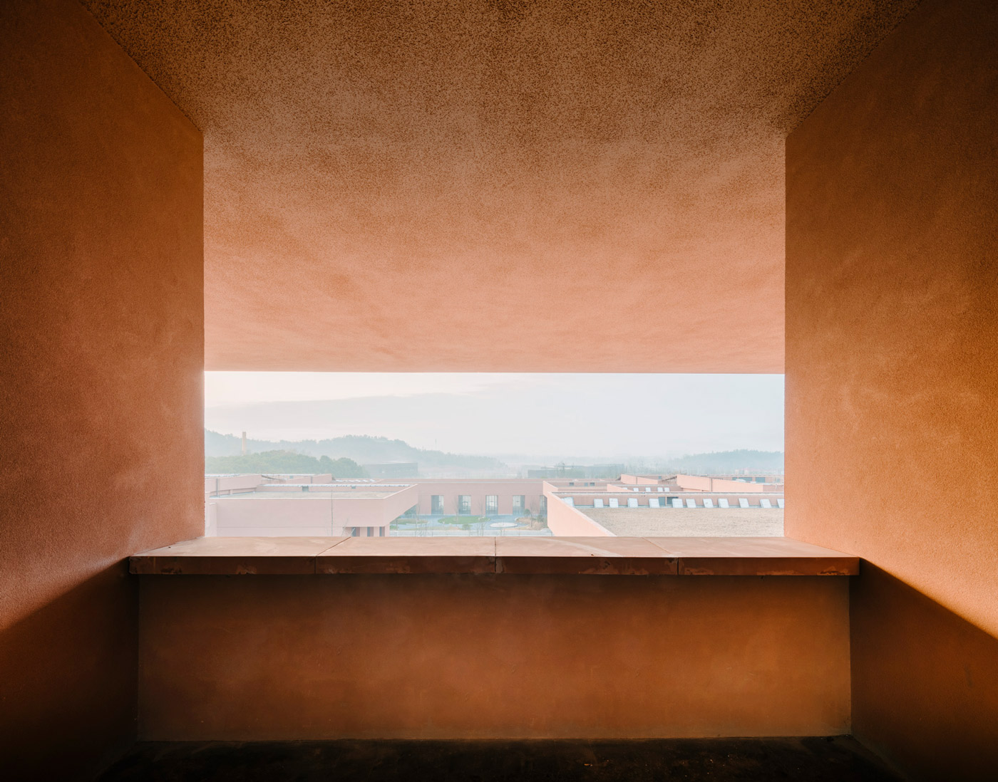 Zhejiang Museum of Natural History by David Chipperfield Architects — A symmetrical portal of rendered concrete frames the landscape beyond, its warm terracotta walls creating a geometric threshold into the valley.