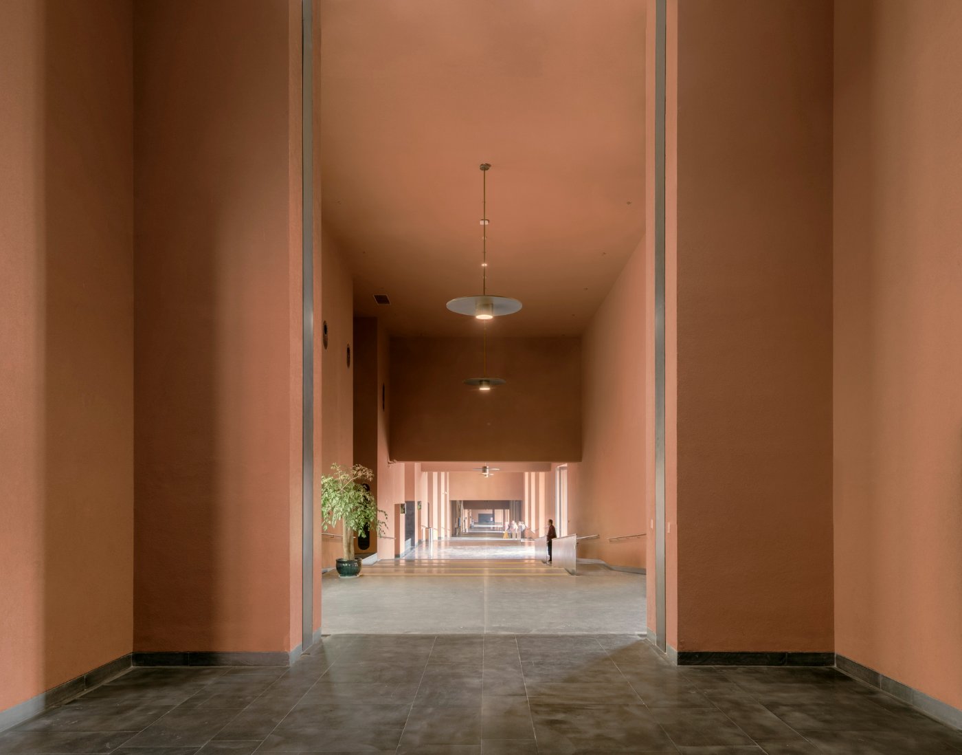Zhejiang Museum of Natural History by David Chipperfield Architects — A symmetrical portal frames the museum's interior passage, defined by two parallel rendered concrete walls in warm terracotta tone rising approximately 3-4...