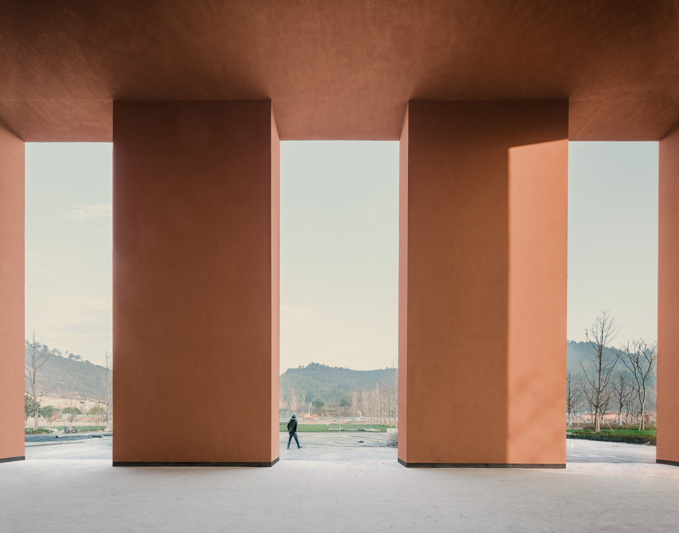 Zhejiang Museum of Natural History by David Chipperfield Architects — Two monolithic rendered concrete walls in terracotta tone frame a symmetrical portal opening onto a landscaped valley.