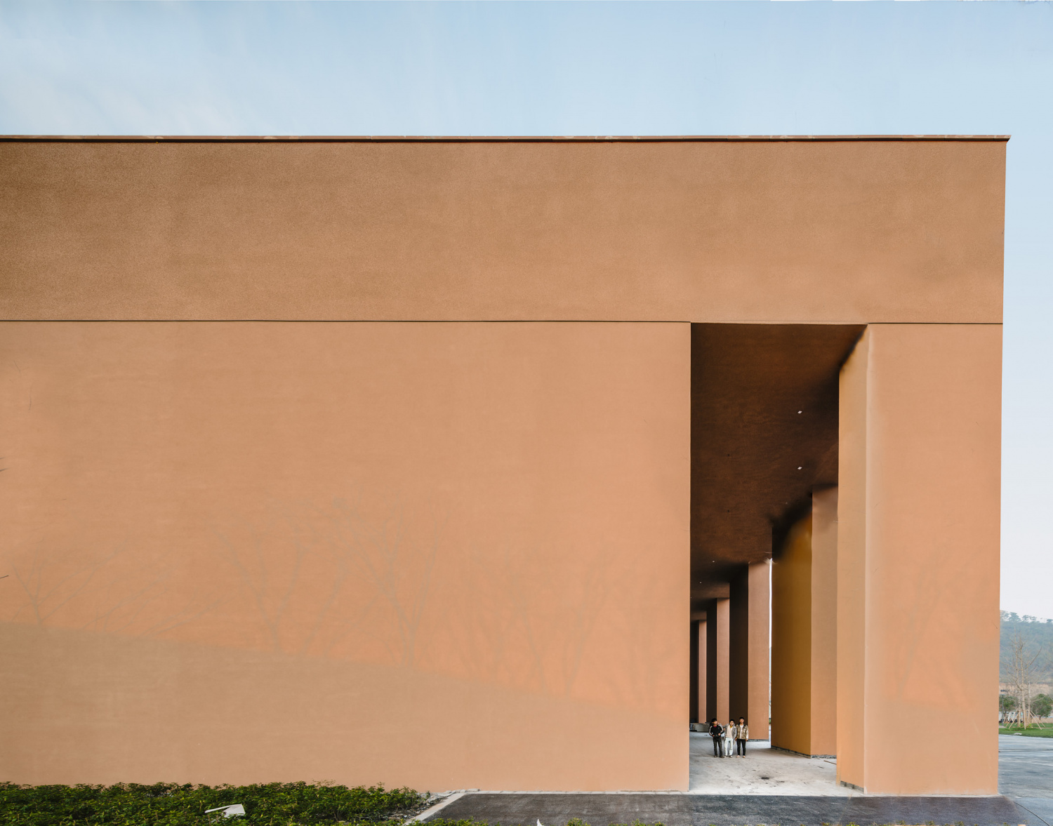 Zhejiang Museum of Natural History by David Chipperfield Architects — Two parallel rendered concrete walls in warm terracotta create a symmetrical portal entrance to the Zhejiang Museum of Natural History.