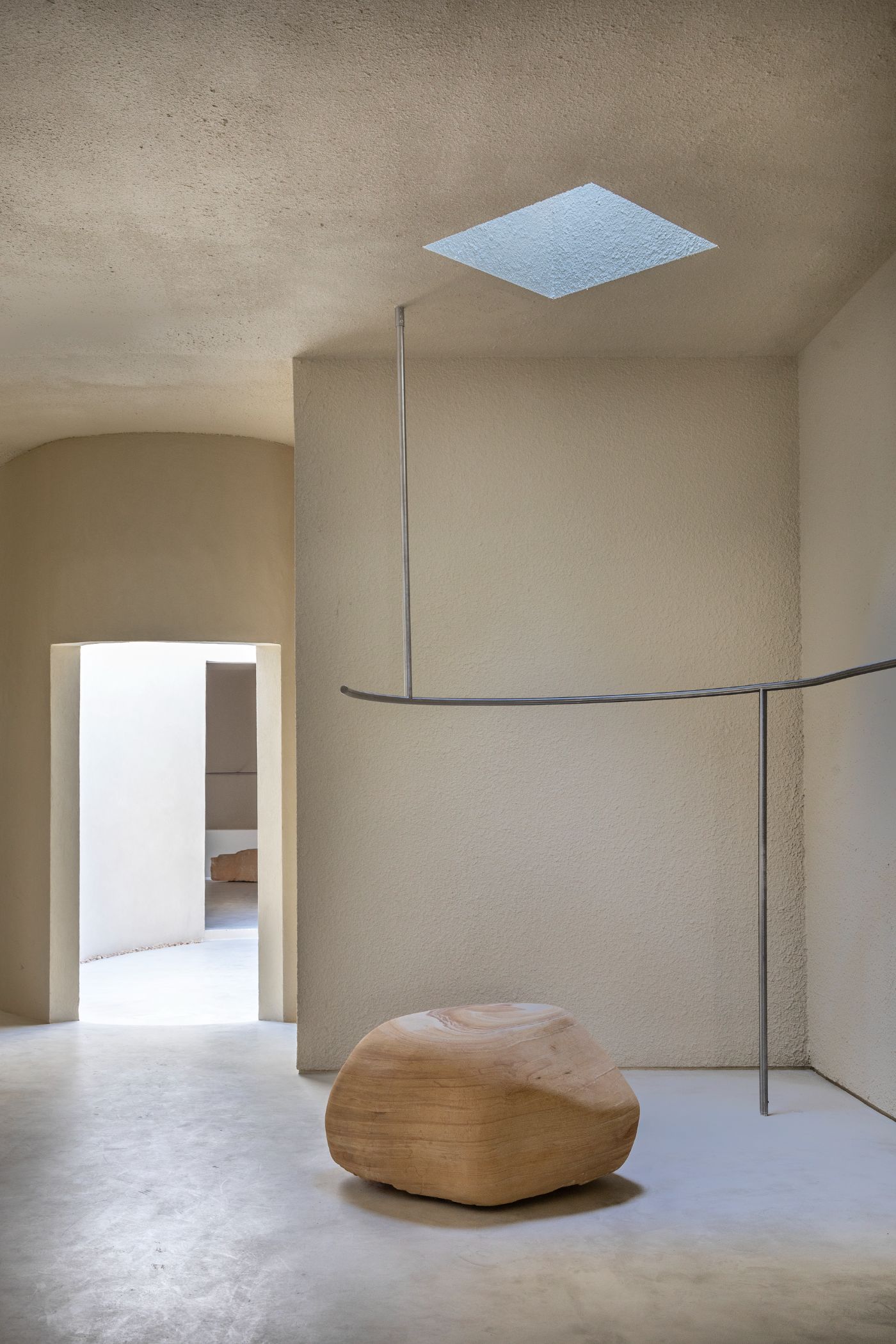 Haight Clothing Store by Entre Terras & Pablo Resende — A single overhead skylight punctures the rendered plaster ceiling, flooding the interior with natural light and establishing a vertical axis through the space.