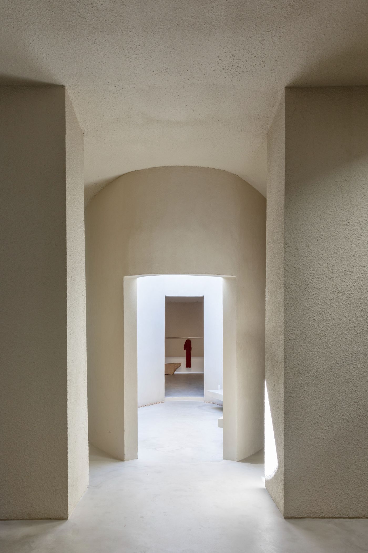 Haight Clothing Store by Entre Terras & Pablo Resende — A rendered plaster corridor with curved barrel-vault ceiling channels light from an overhead opening, creating a bright vertical passage.