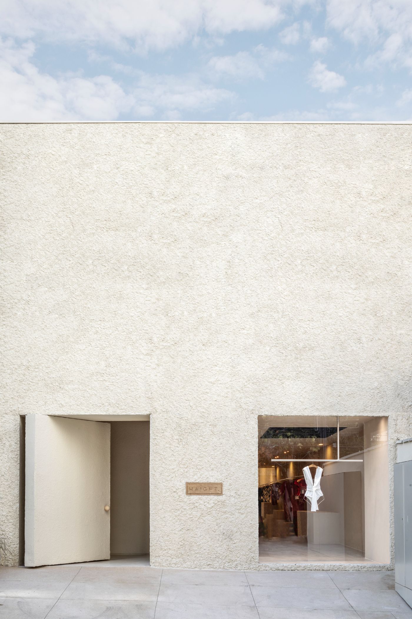 Haight Clothing Store by Entre Terras & Pablo Resende — The storefront presents a studied composition of material contrasts across a rendered plaster facade.