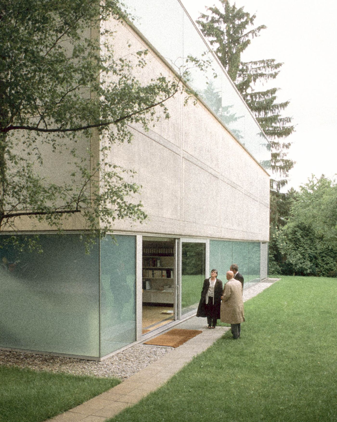 Sammlung Goetz by Herzog & de Meuron — Two visitors approach the Sammlung Goetz gallery across a manicured lawn, framing the building's layered horizontal composition.