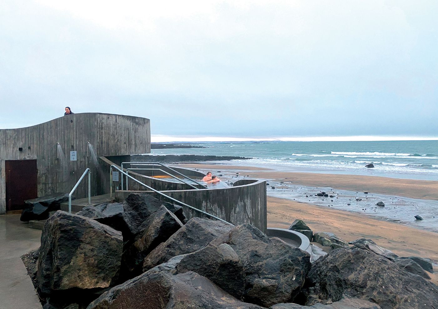 Guðlaug Baths by BASALT Architects — Guðlaug Baths by BASALT Architects in Akranes, Iceland, shows the weathered timber-clad cylindrical structure positioned directly against natural granite...