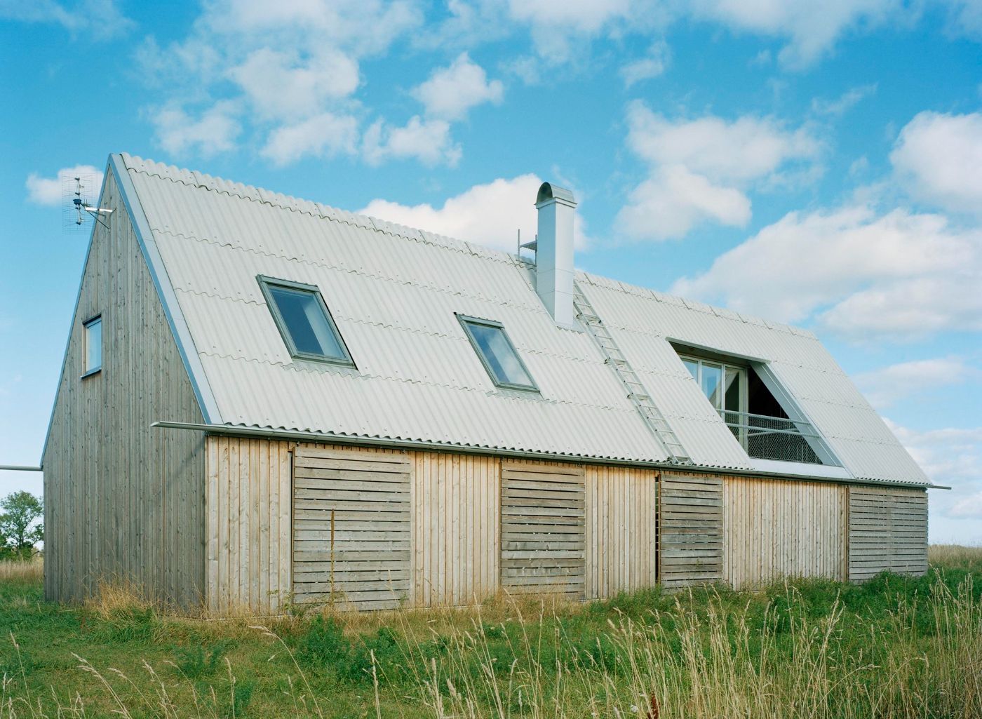 Sommarhus at Stora Gasmora by LLP Arkitektkontor — A gabled summer house clad in weathered larch timber boards, set against a Baltic plateau landscape.