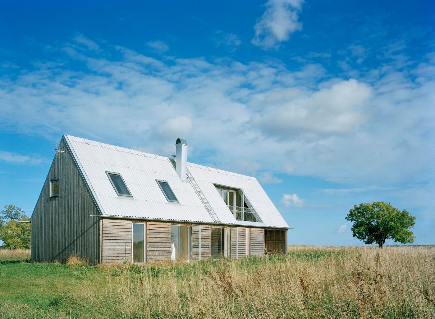 Sommarhus at Stora Gasmora by LLP Arkitektkontor — A pitched-roof dwelling sits isolated across open meadowland, its gabled form referencing rural agricultural vernacular.