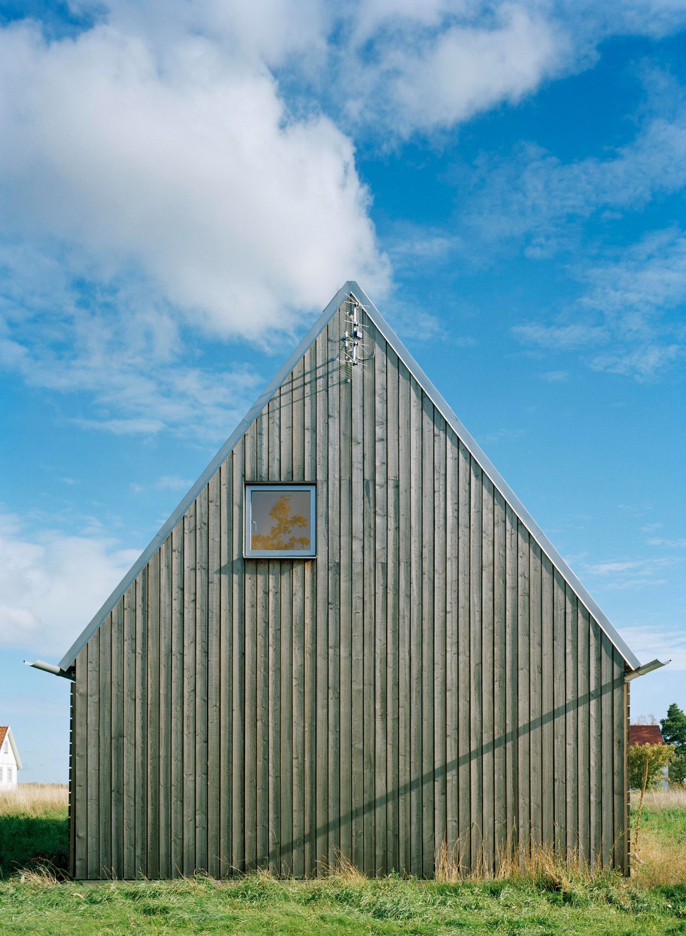 Sommarhus at Stora Gasmora by LLP Arkitektkontor — A pitched-roof timber structure clad in weathered larch boards faces the camera in frontal symmetry.