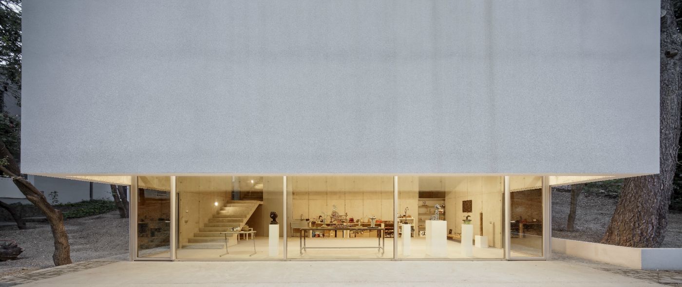 Arranz Bravo Studio by Garcés - De Seta - Bonet Arquitectes — A monolithic rendered structure with a pitched roof sits nestled within a grove of tall eucalyptus trees, its white facade unbroken except for an expansive...