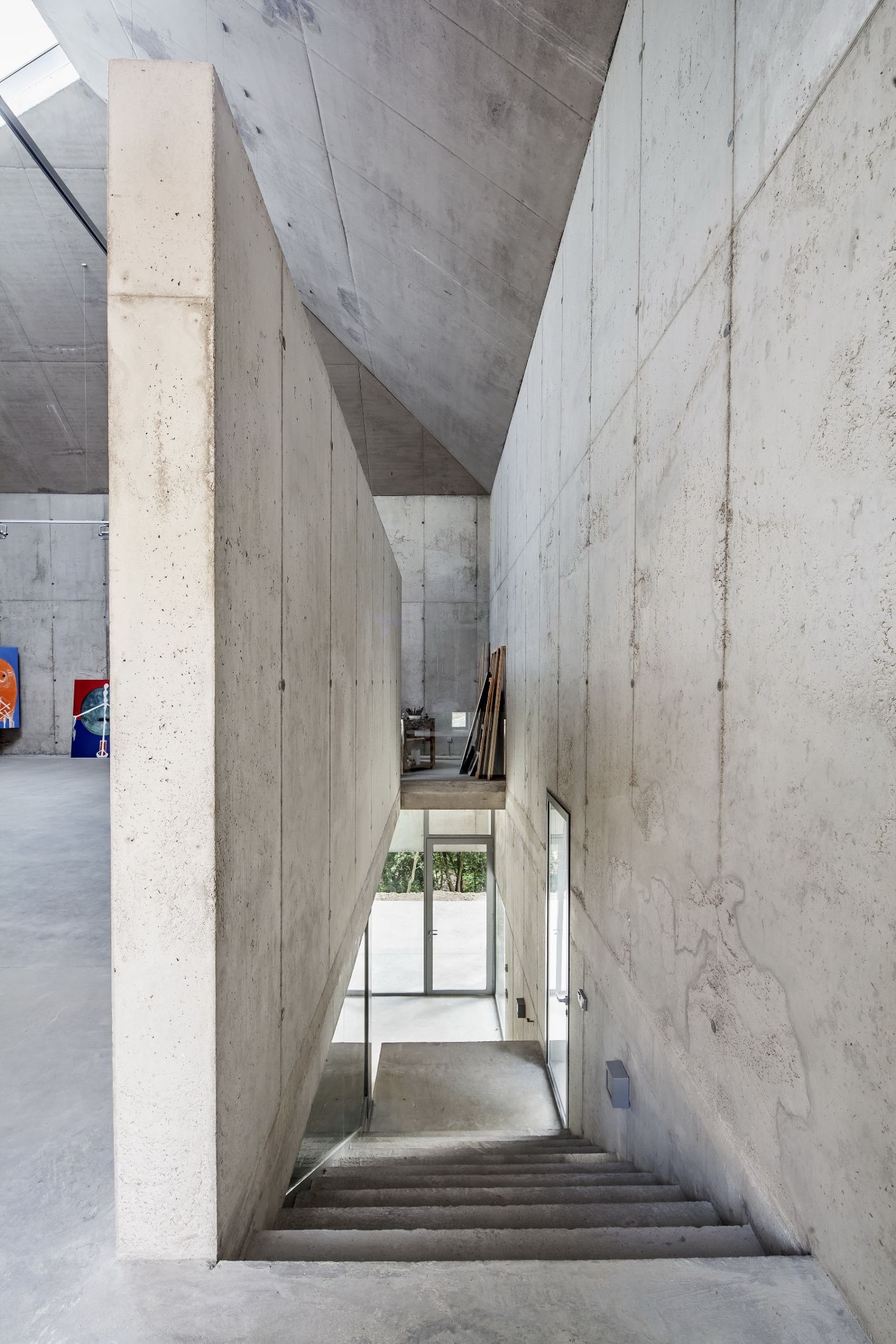 Arranz Bravo Studio by Garcés - De Seta - Bonet Arquitectes — A narrow concrete corridor descends between two monolithic board-formed concrete walls, their surfaces marked by formwork seams and weathering stains.