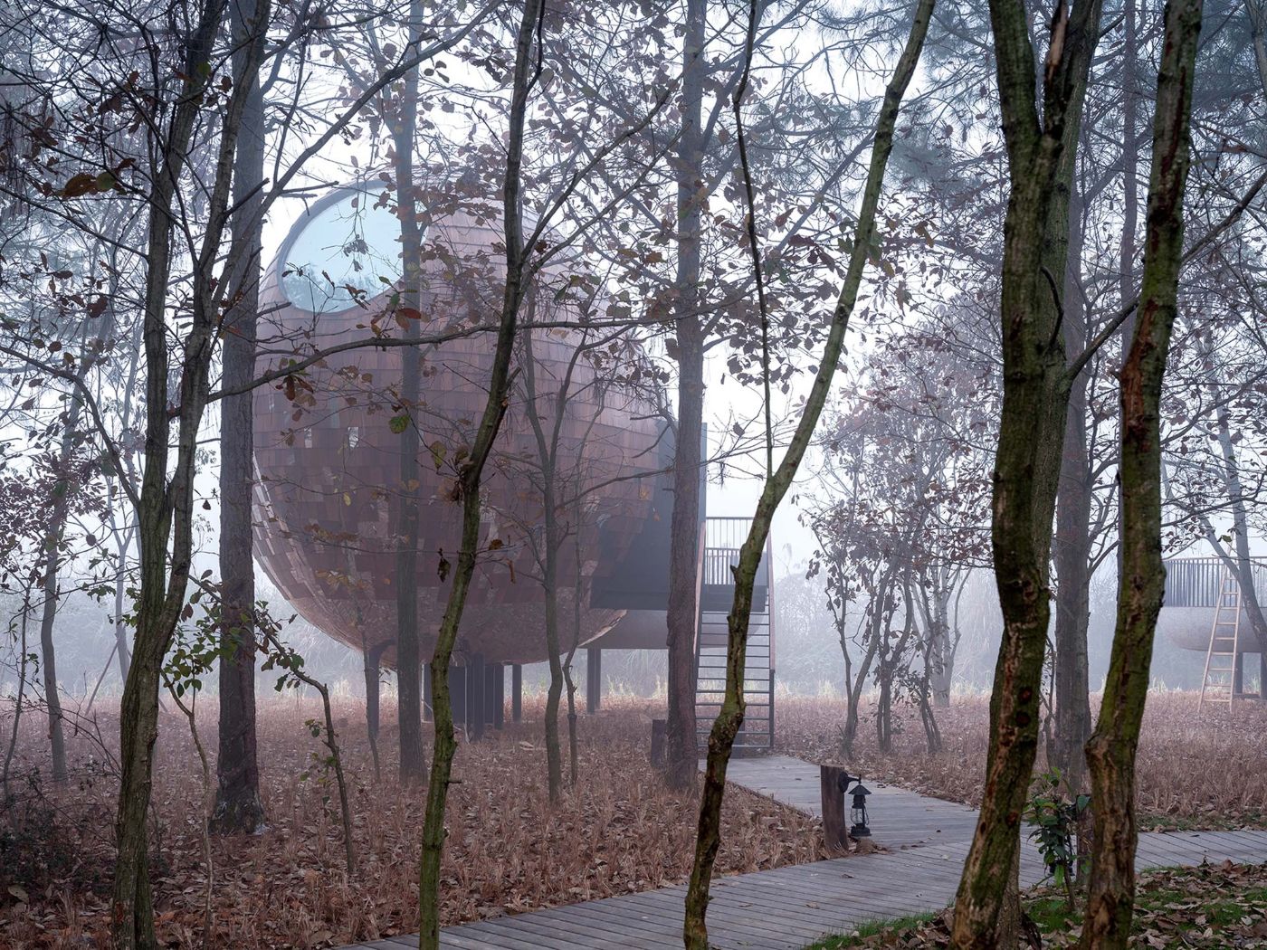 The Seeds Houses by ZJJZ Atelier — A monolithic ellipsoidal structure clad in mirrored aluminum tiles rises among bare deciduous trees, its reflective upper surface fragmenting views of the...