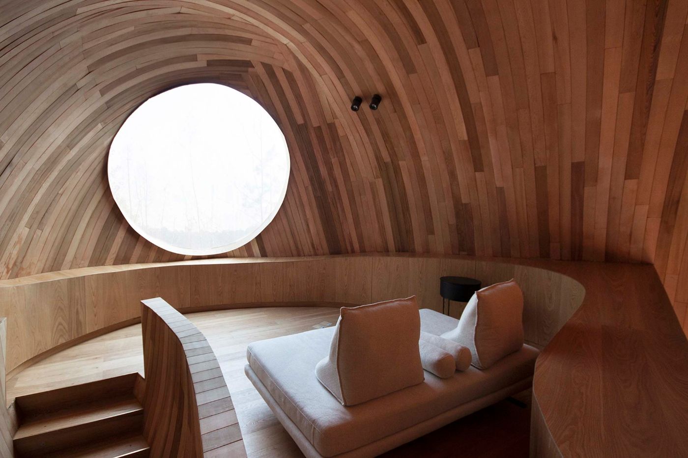 The Seeds Houses by ZJJZ Atelier — A wood-lined interior chamber features concentric curved timber elements that create a vaulted tunnel effect, with horizontal planks graduating in tone from...