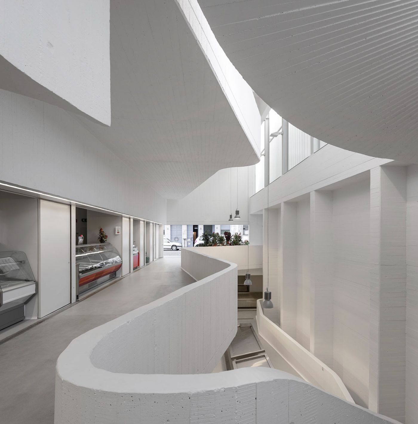 Abrantes Municipal Market by ARX Portugal — A spiraling concrete cylinder anchors the market's interior, its board-formed surface texture visible as it rises through multiple levels.