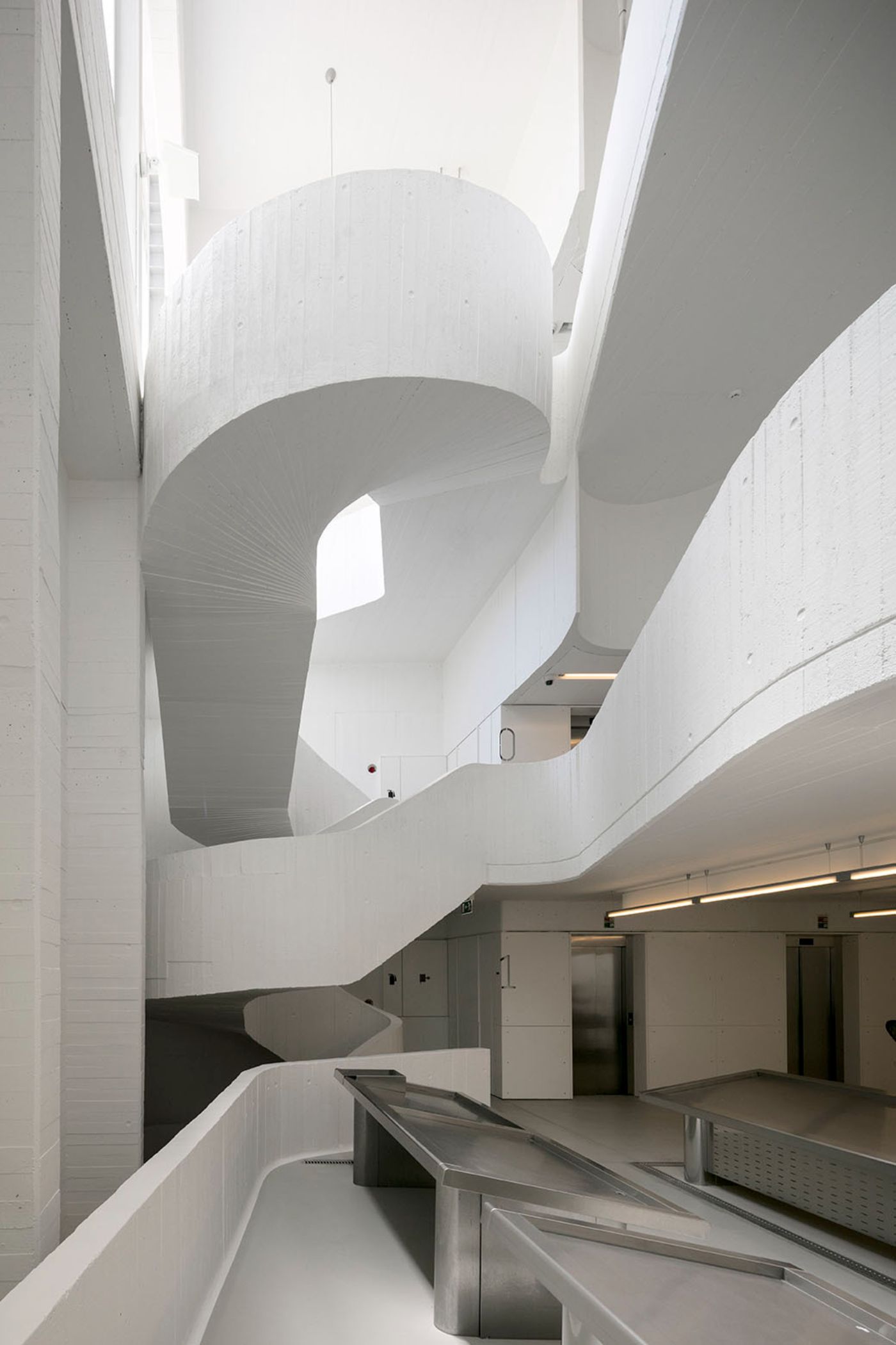 Abrantes Municipal Market by ARX Portugal — A cylindrical concrete spiral rises through multiple floor levels, its board-formed surface revealing aggregate texture and construction seams.