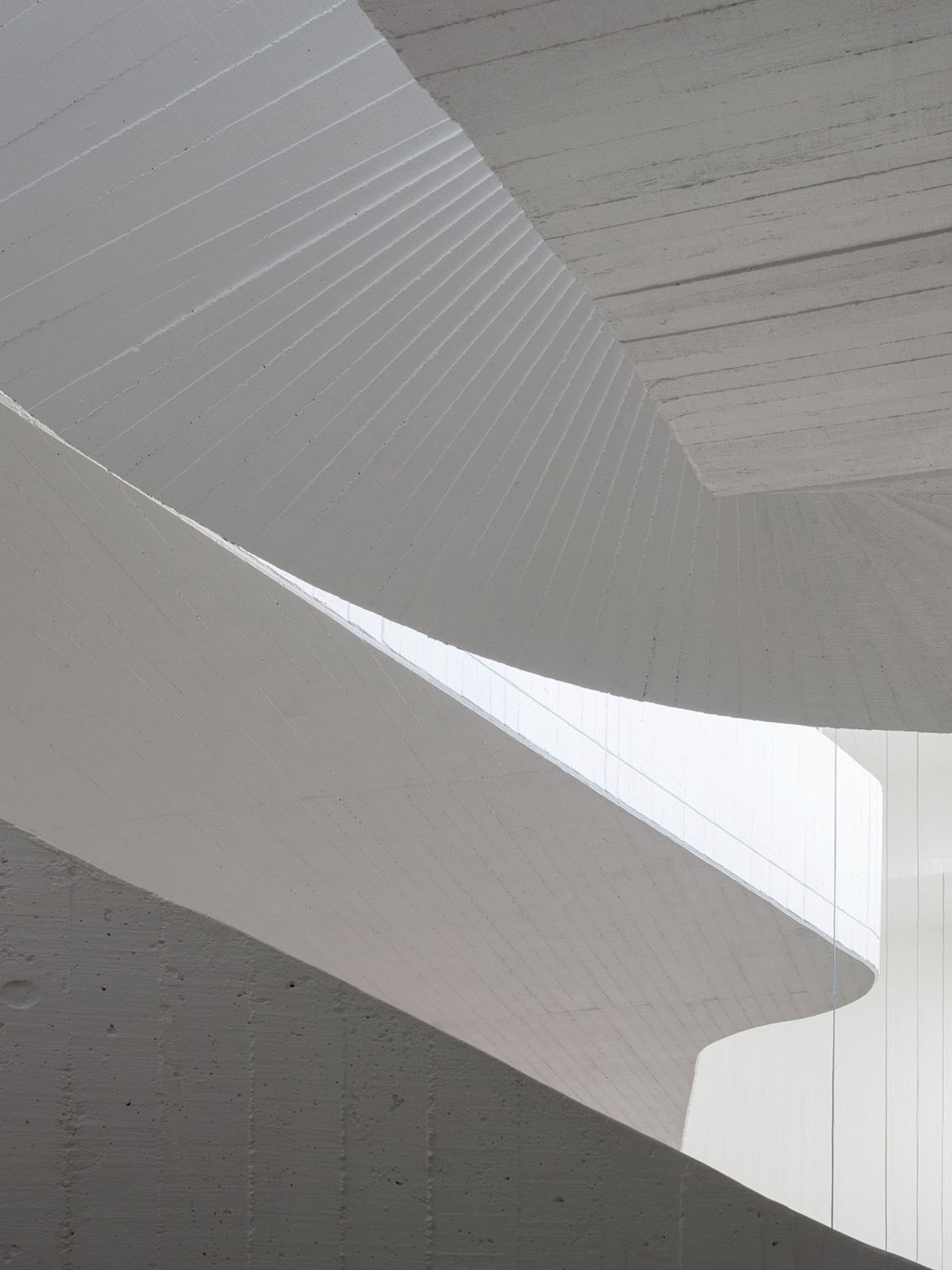 Abrantes Municipal Market by ARX Portugal — A spiral concrete ramp ascends through the market's interior void, its cylindrical form captured from above in sharp geometric perspective.