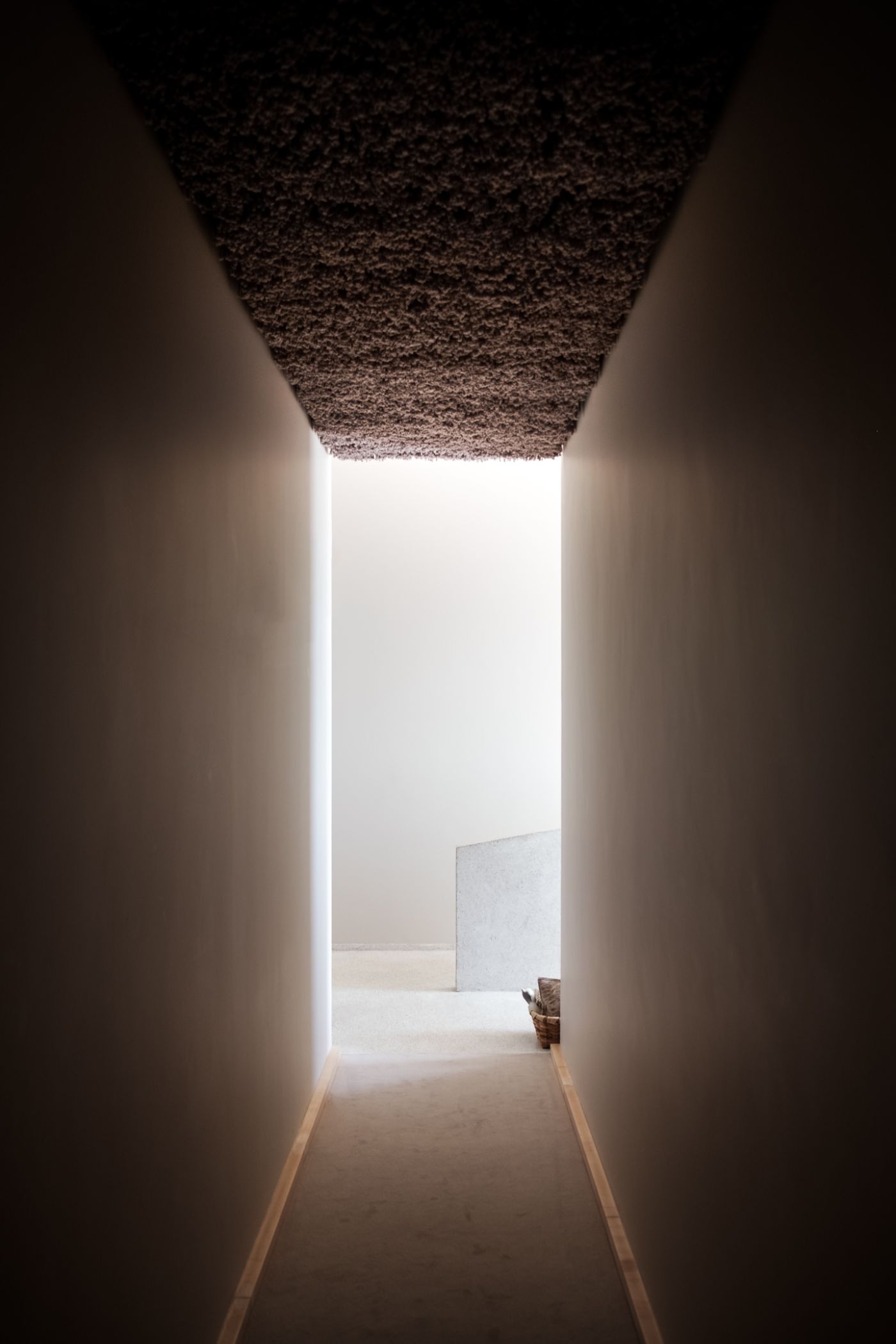 Casa de São Lourenço by P-06 Atelier and Site Specific by P-06, Site Specific, Rogério de Azevedo — A narrow corridor frames the passage between two rendered concrete walls, their surfaces uniformly cream-colored.