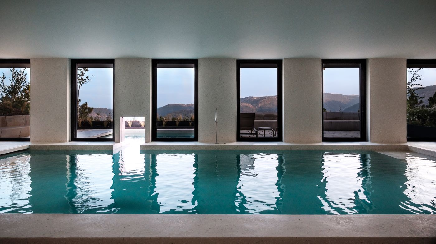 Casa de São Lourenço by P-06 Atelier and Site Specific by P-06, Site Specific, Rogério de Azevedo — An interior swimming pool viewed lengthwise along its turquoise water, framed by a repetitive grid of black-framed glass doors and cream-colored...