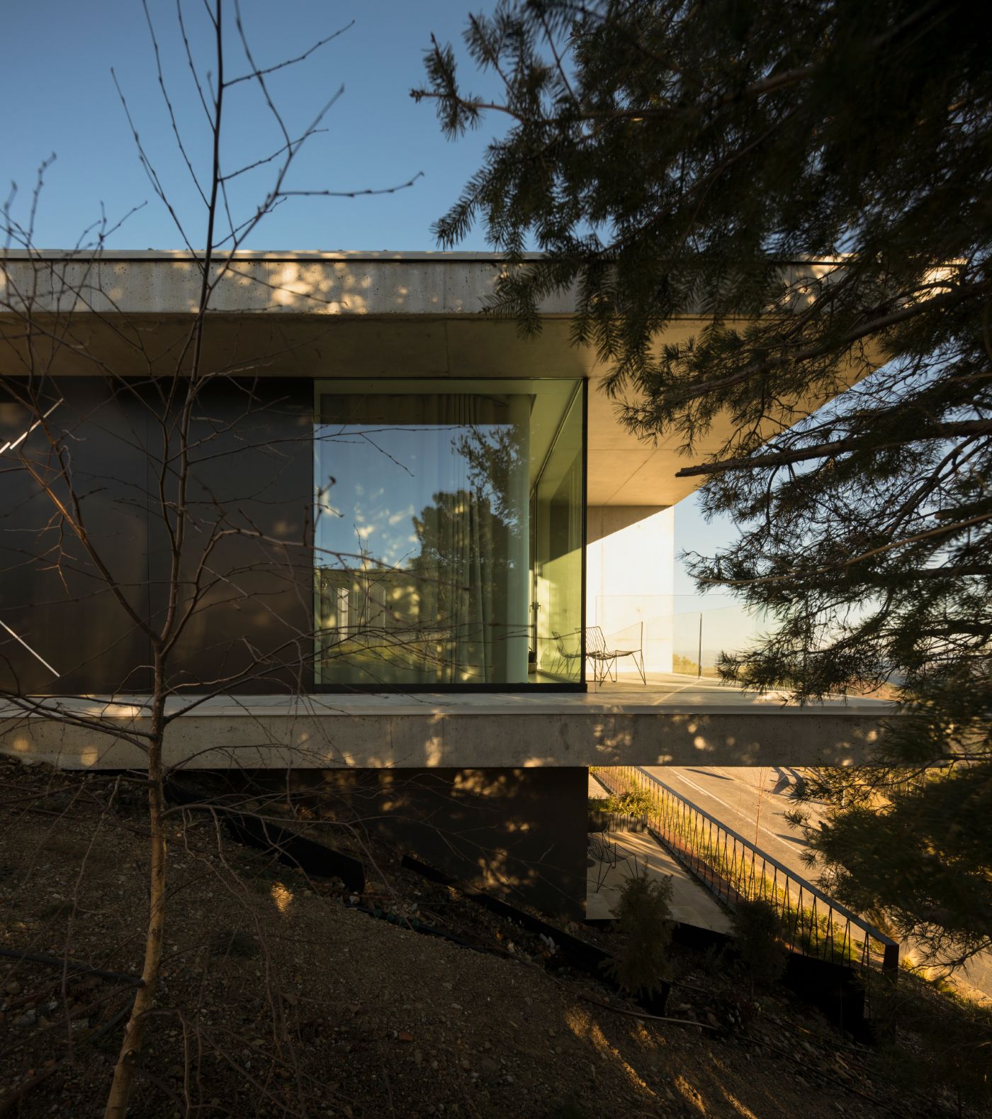 Casa de São Lourenço by P-06 Atelier and Site Specific by P-06, Site Specific, Rogério de Azevedo — A modernist pavilion elevated on pilotis, its facade defined by a recessed grid of white-painted concrete mullions framing deep blue-tinted glazing.