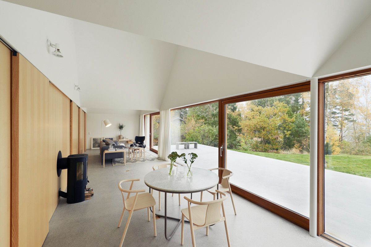 Summerhouse Lagnö by Tham & Videgård Arkitekter — The interior dining space anchors the open-plan living area, with a white oval table and light timber chairs positioned to command views through the...