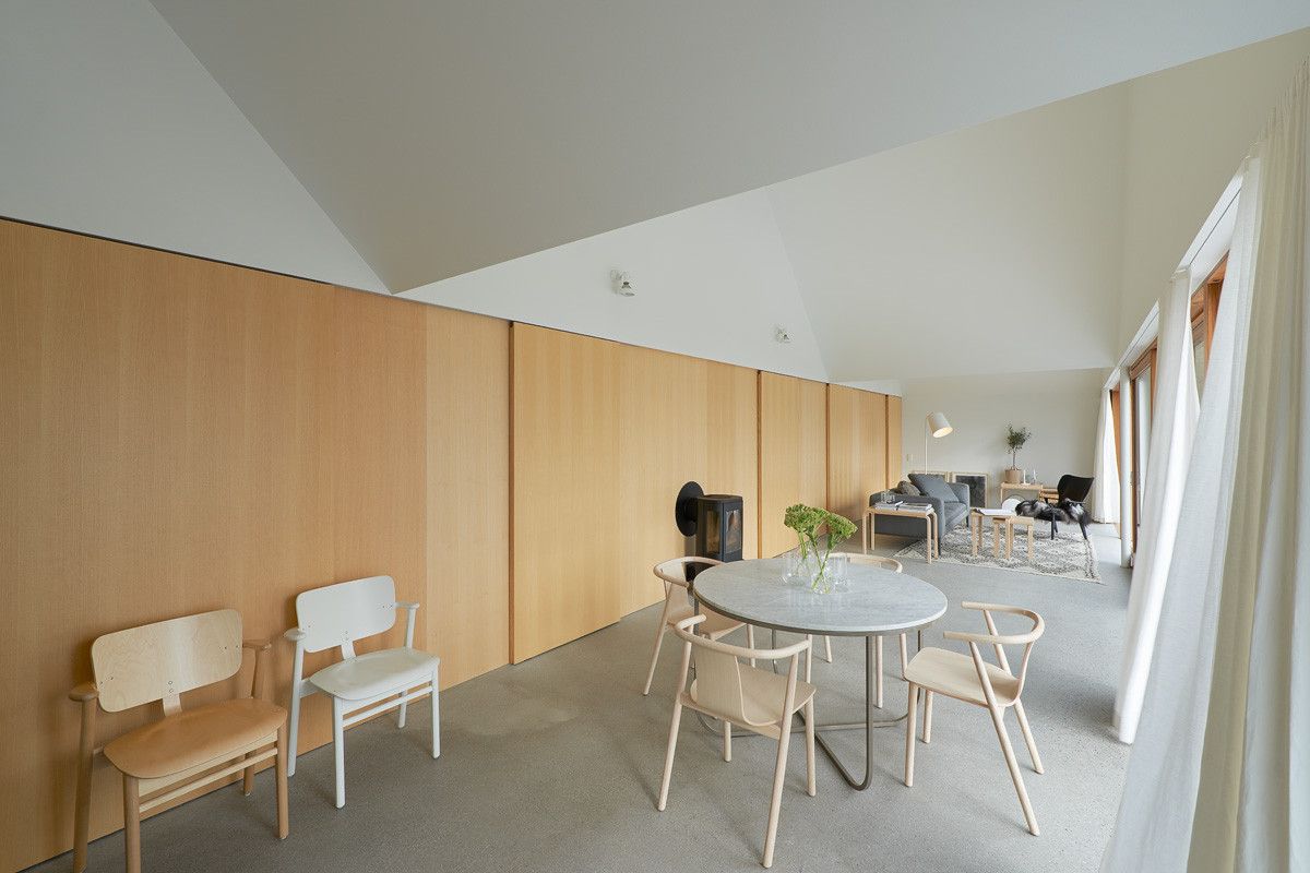 Summerhouse Lagnö by Tham & Videgård Arkitekter — The interior social zone of Summerhouse Lagnö features a central dining area beneath the pitched gable roof, with a circular stone-topped table surrounded...