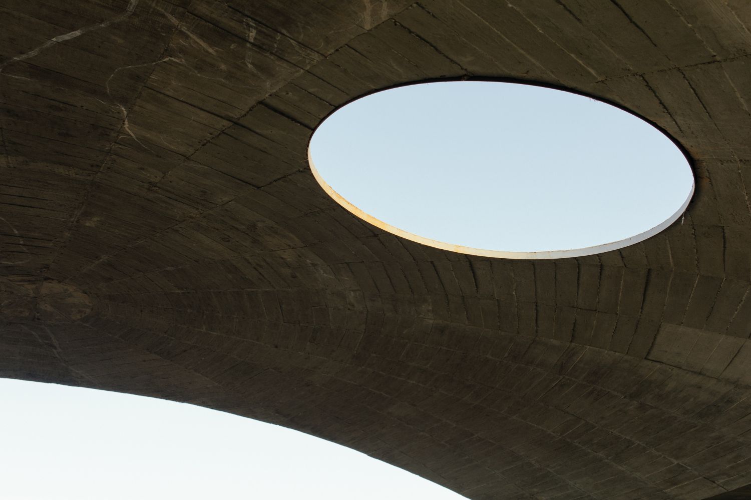 Casa na Terra captured by Thisispaper Studio — Overhead view of Casa na Terra's defining architectural gesture: a circular white skylight pierces the dark concrete roof plane, its golden edge catching...