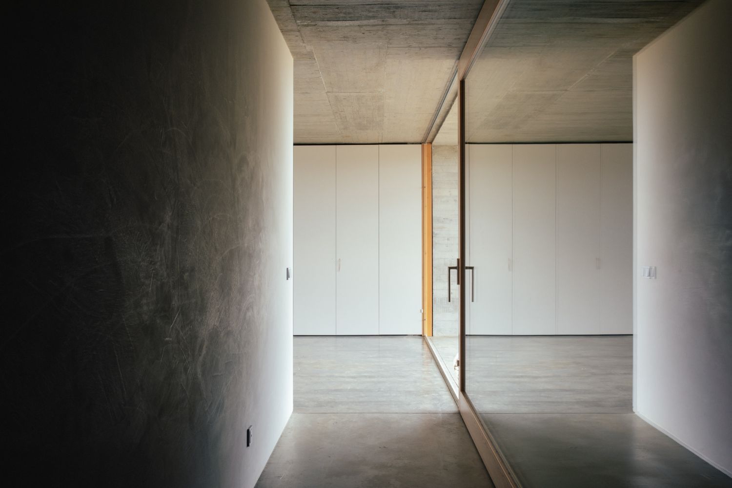 Casa na Terra captured by Thisispaper Studio — Interior passage framed through a timber-lined doorway reveals a minimalist gallery space defined by board-formed concrete ceiling and white plaster walls.
