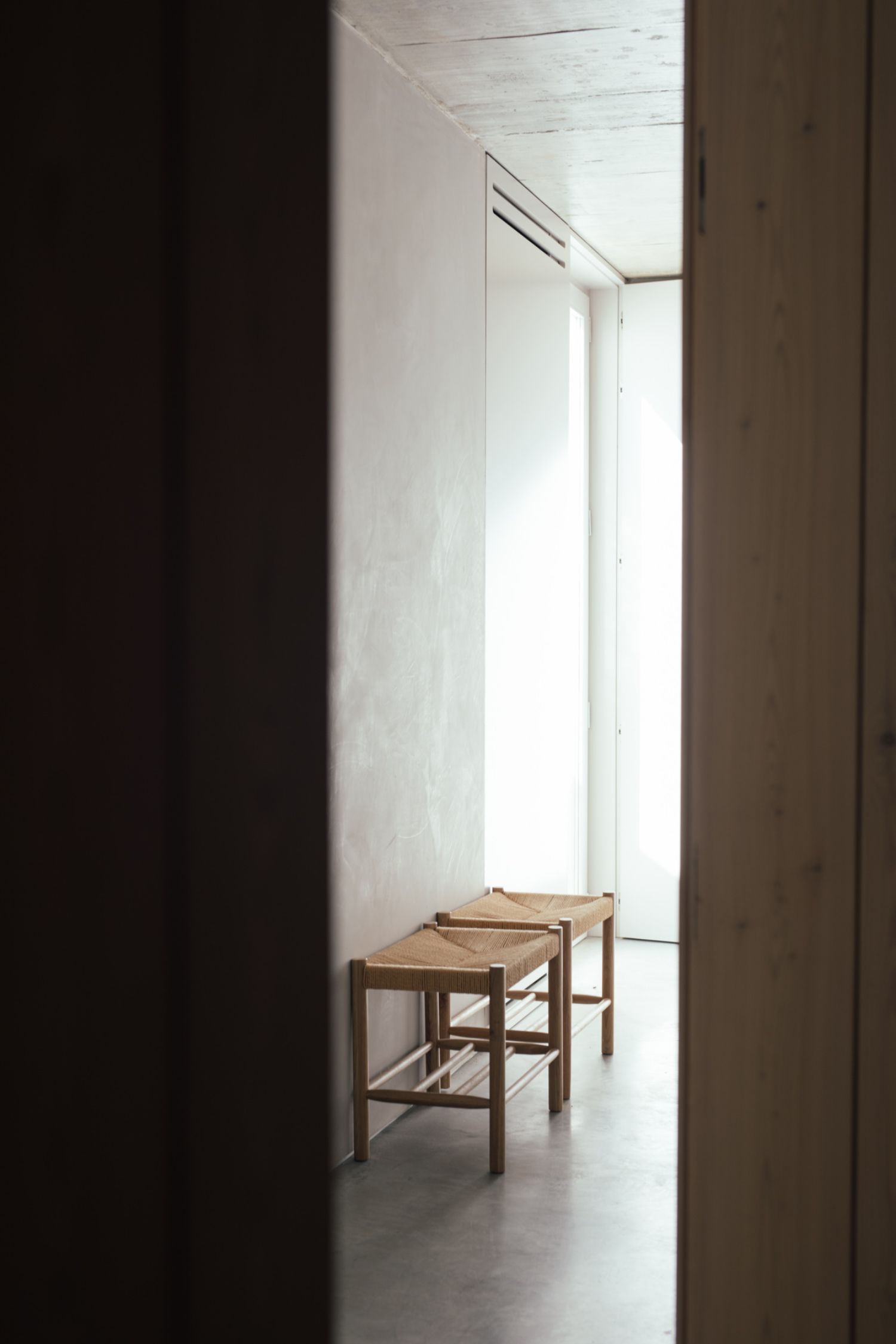 Casa na Terra captured by Thisispaper Studio — A narrow corridor framed by dark timber walls creates a controlled perspective toward a bright interior space.
