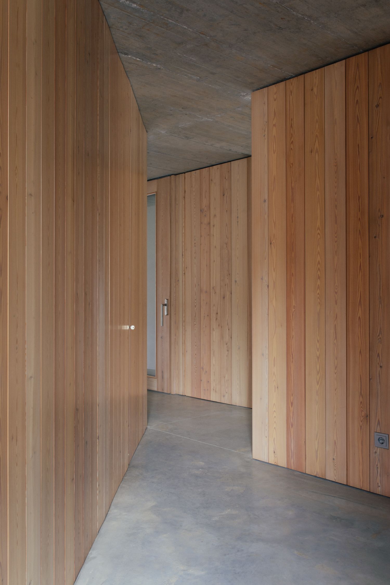 Casa na Terra captured by Thisispaper Studio — Interior passage of Casa na Terra reveals the architect's material and spatial strategy through a compressed corridor lined with timber-clad walls in warm...