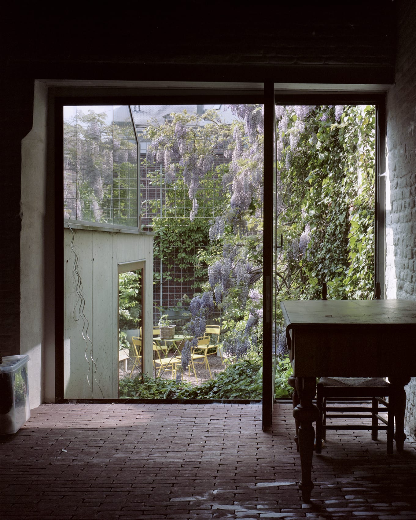 ‘Room in the City’ by 51N4E — View from interior concrete room through large glazed threshold into densely planted courtyard.