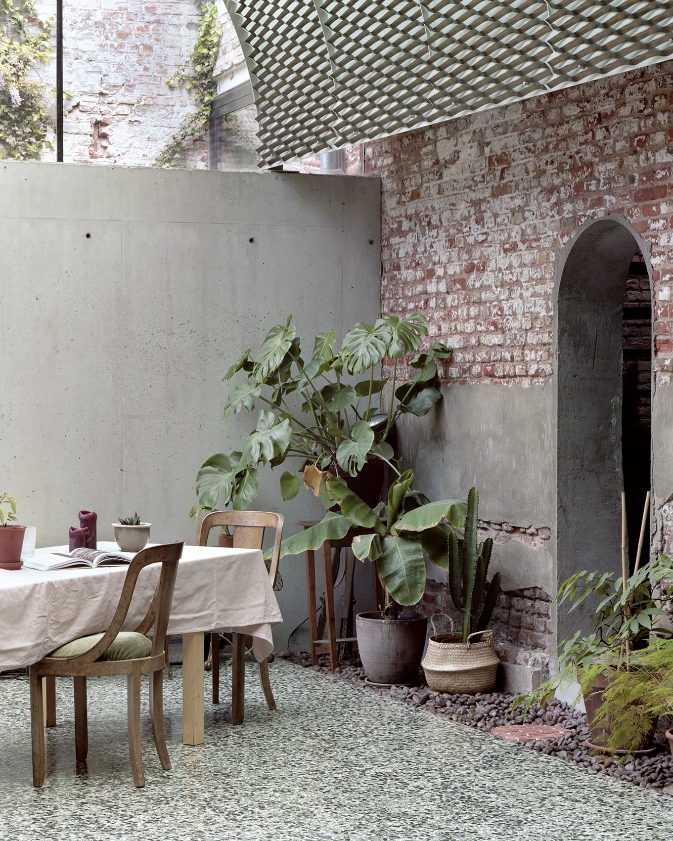 ‘Room in the City’ by 51N4E — A threshold space anchors the composition: concrete interior wall on the left, exposed brick courtyard on the right.
