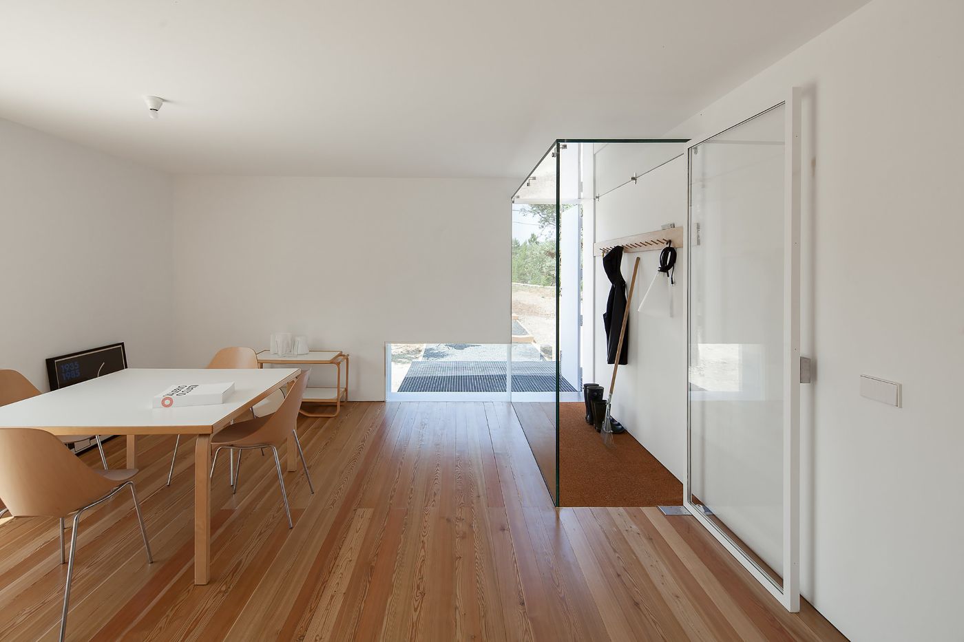 Fonte Boa House by João Mendes Ribeiro — Interior view of Fonte Boa House showing the dining area with a light wood table and natural leather chairs positioned on timber flooring.