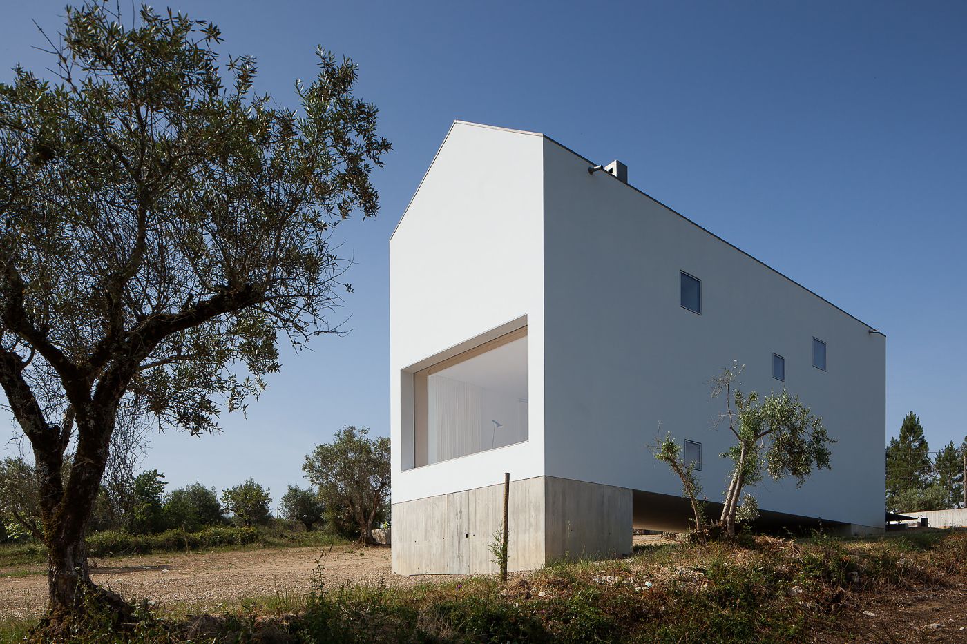Fonte Boa House by João Mendes Ribeiro — The Fonte Boa House presents a bipartite composition: a rendered white upper volume containing a large horizontal strip window sits atop a raw concrete...