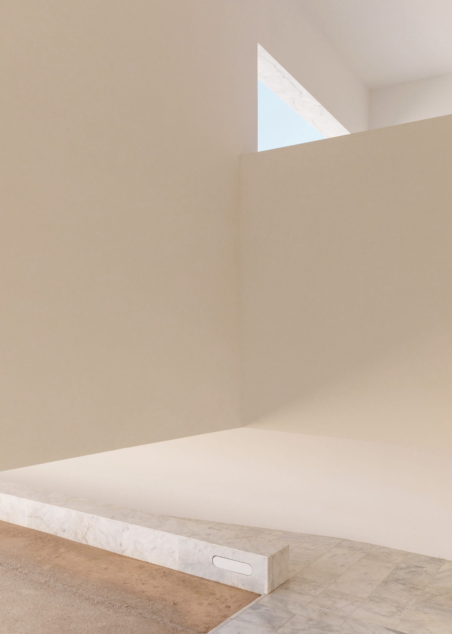 Grândola’s Library and Municipal Archive by Matos Gameiro Arquitectos + Pedro Domingos Arquitectos — A rendered white interior wall rises from a travertine plinth punctuated by a single recessed horizontal opening.