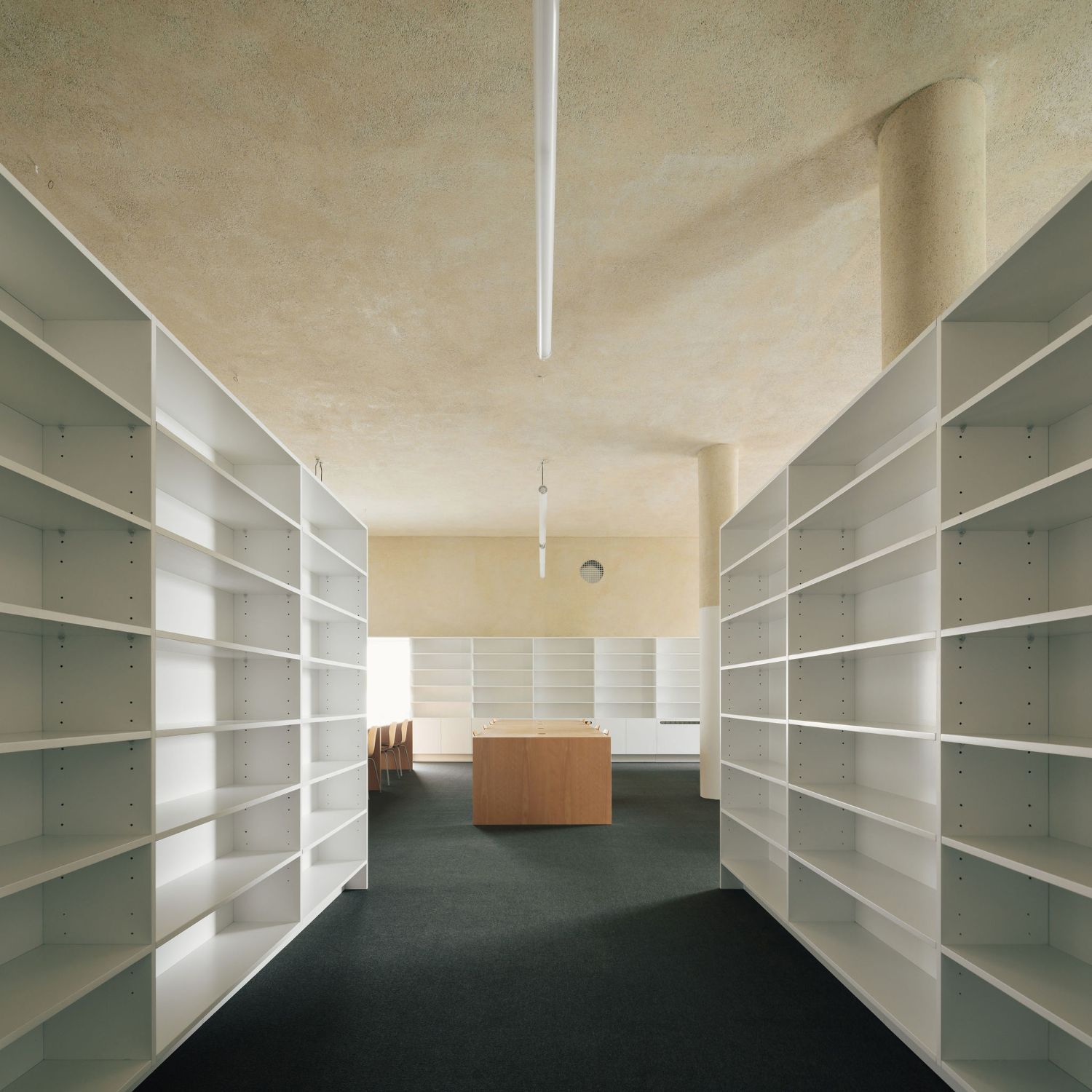 Grândola’s Library and Municipal Archive by Matos Gameiro Arquitectos + Pedro Domingos Arquitectos — The library's interior archive corridor stretches in linear perspective, flanked by symmetrical white modular shelving units with adjustable metal pegs.